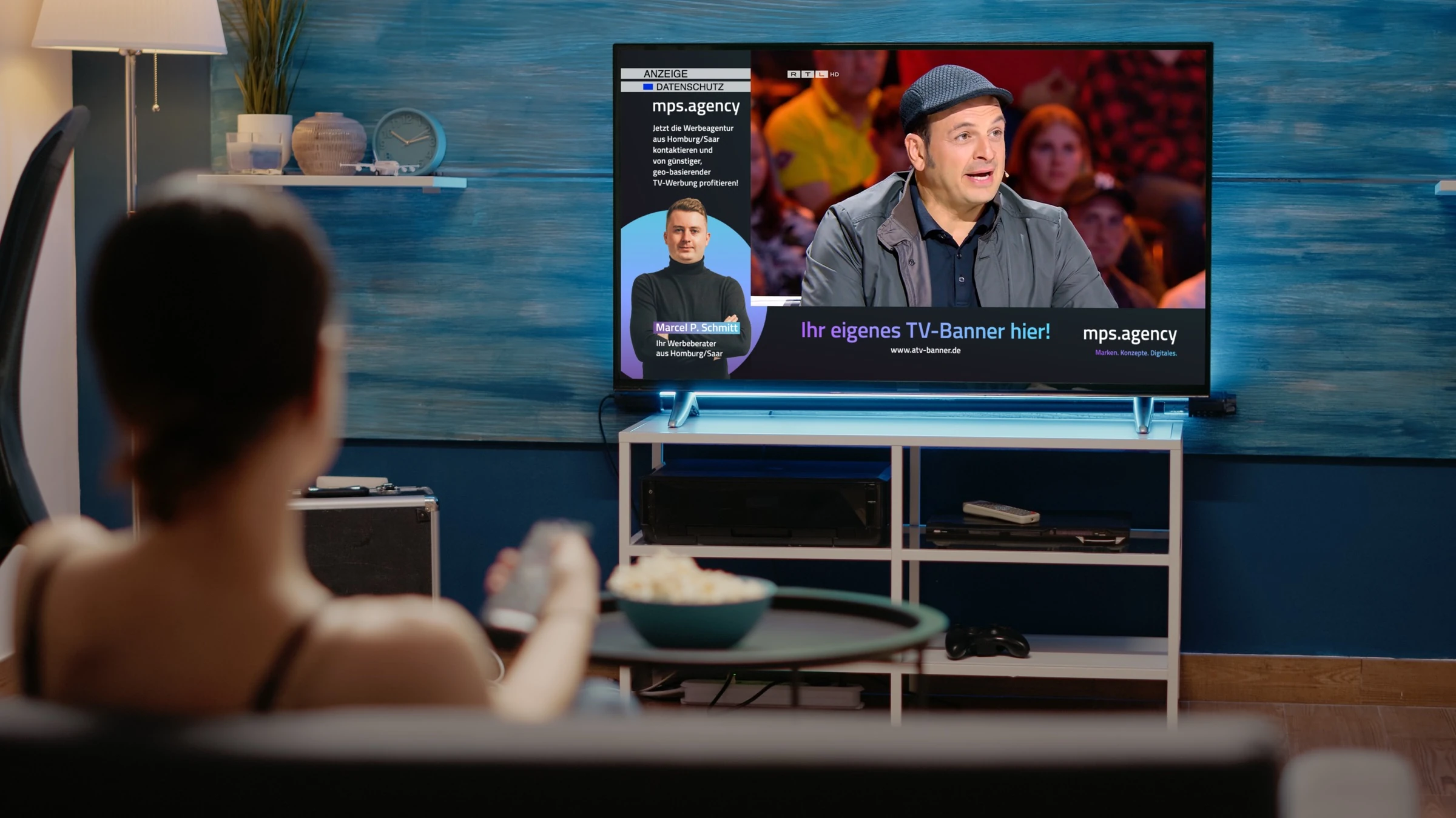 Zuschauerin im Wohnzimmer vor einem Smart-TV, auf dem ein ATV-Banner in L-Form von mps.agency neben dem laufenden Programm eingeblendet ist