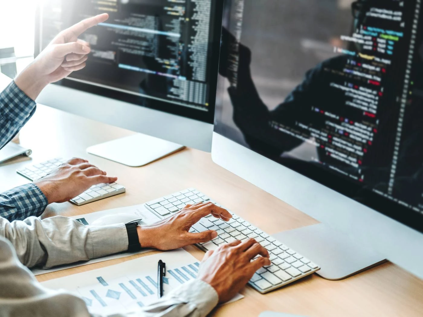 Zwei Entwickler arbeiten an Monitoren mit Code und Auswertungen