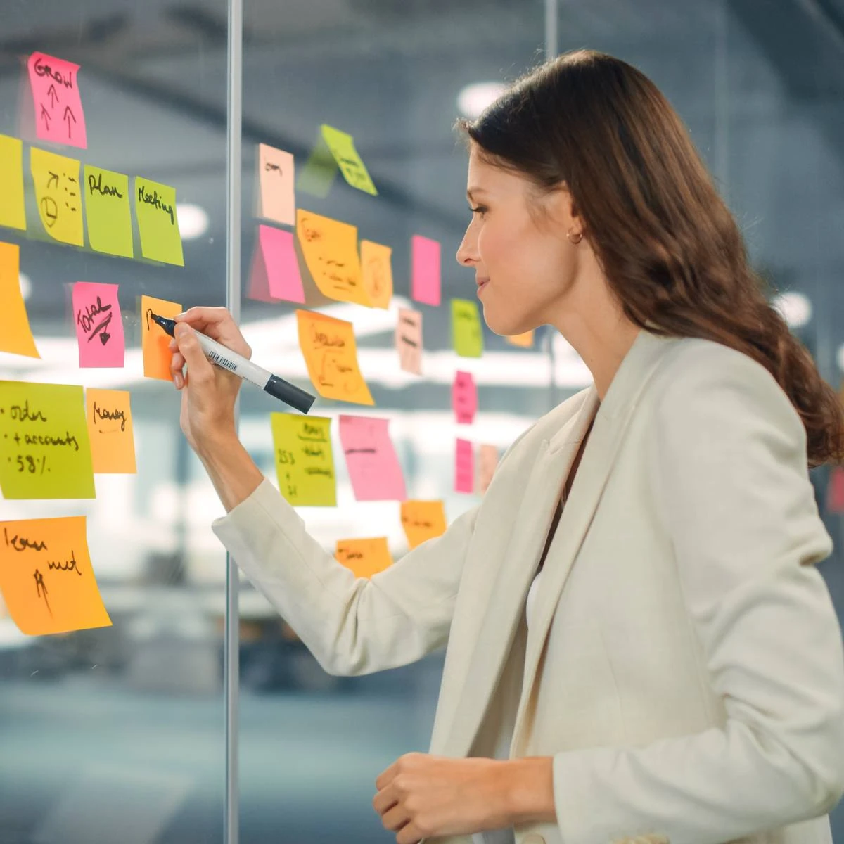 Strategin sortiert Notizzettel an einer Glaswand während eines Marken-Workshops